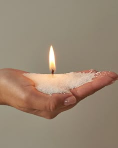 a person holding out their hand with a small candle in the middle of it and salt on top