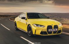 a bright yellow sports car driving down the road with dark clouds in the sky behind it