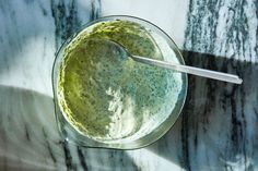 a glass bowl filled with green liquid on top of a marble counter next to a spoon