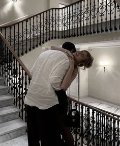 a man and woman hug on the stairs in front of a staircase case with wrought iron railings