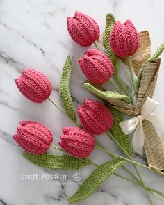 pink crocheted flowers with green stems on a white marble countertop next to a ribbon