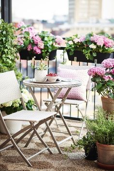 two chairs and a table on a balcony with potted flowers in the background,