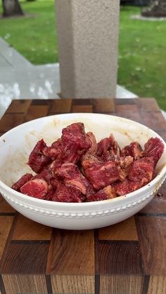 a white bowl filled with meat sitting on top of a wooden table next to a stone pillar