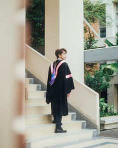 a young man standing on the steps in front of a building wearing a graduation gown