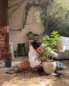 a woman kneeling down next to a potted plant