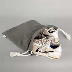 a pair of white sneakers sitting on top of a gray floor next to a drawstring bag