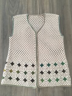 a white crocheted vest with green and black stars on the front, sitting on top of a wooden floor