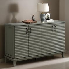 a sideboard with two doors and a lamp on it in a room that has beige walls