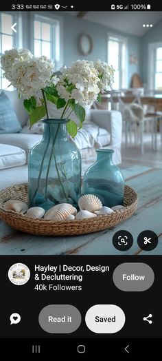 a blue vase with white flowers and seashells in it on a wooden table