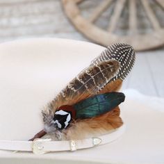 Elevate your hat game with this feather accent, featuring natural guinea and iridescent feathers. Finished with a ribbon on the tail, it tucks neatly into any hat band for a secure fit. Perfect for adding personality to your favorite hat—hat not included. Make a statement with this unique accessory! Natural Feathers Approx. 8 inches - sizes may vary slightly Tuck into the band of any hat! *Hat not included* Prop 65 Warning ↗️ Adjustable Brimmed Hat With Feathers, Country Style Hats With Feathers For Western-themed Events, Feather Hat Accent, Feathered Hat Bands For Western-themed Events, Adjustable Feather Trim Hat For Western-themed Events, Beaded Hat Bands, Kids Belt, Outdoor Hats, Beaded Hat