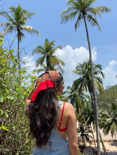 a woman wearing a red bandana standing in front of palm trees on the beach