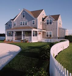 a large house sitting on top of a lush green field next to a white picket fence