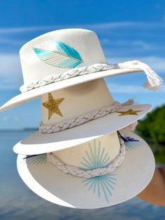 Beautiful white jute hats with sewn thread designs. Loving our gold stars, blue feather, starburst designs. Sombreros Decorados Ideas, Felt Hats, Trendy Hat, Fancy Hats, Blue Feather, Western Hats, Hat Box, Felt Hat, Custom Hats