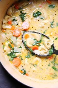 a pot filled with pasta, carrots and spinach soup on top of a table