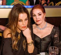 two women sitting next to each other in front of a table with wine glasses on it