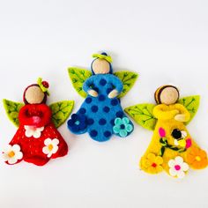 three little felt angels sitting next to each other on a white surface with flowers and leaves