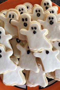 cookies decorated with white icing and black candies are arranged on an orange plate