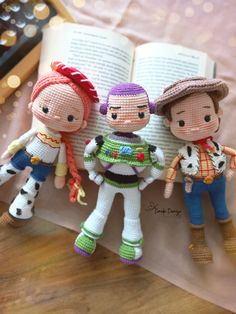 three toy dolls are posed next to an open book