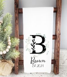 a white towel with the letter b on it next to a potted plant and wooden ladder