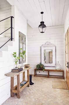 a hallway with white walls and wood flooring has a mirror on the wall next to a bench