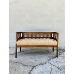 a wooden bench sitting in front of a white brick wall and cement floored area