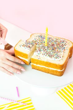 a person holding a piece of cake with a lit candle on it and sprinkles