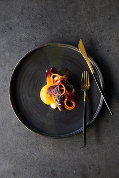 a black plate topped with food next to a fork and knife on top of a table