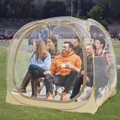 a group of people sitting inside of a tent on top of a field with grass