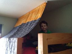 a young boy standing on top of a wooden bunk bed under a canopy over his bed