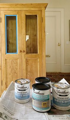 three paint cans sitting on top of a table next to a wooden cabinet and newspaper