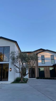 a large white house with lots of windows and trees in the front yard at dusk