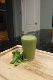 a green smoothie sitting on top of a wooden cutting board