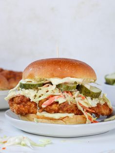 a chicken sandwich with coleslaw and pickles on a plate next to some bread