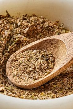 a wooden spoon in a bowl filled with dried herbs and ground flakes on the side