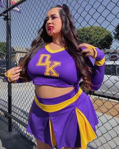 a woman in a purple and yellow cheerleader outfit standing next to a chain link fence