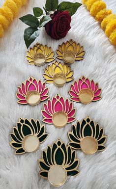 six lotus flower brooches sitting on a white furnishing next to a red rose