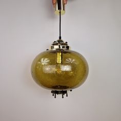 a hand holding a light fixture in the shape of a round glass ball hanging from a wire