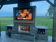 Tombstone DIY Fireplace design by Backyard Flare. TV on fireplace with wood storage boxes voids on sides. Small hearth seating in front of firebox. Green grass behind fireplace and pergola above fireplace. Diy Outdoor Fireplace With Tv, Outdoor Fireplace Tv Wall, Backyard Tv Ideas Patio, Outdoor Fireplace With Tv, Fire Pit Chimney, Fireplace Plans, Veneer Fireplace, Outdoor Fireplace Plans, Outdoor Decks