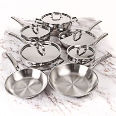 an assortment of stainless steel pots and pans on a marble countertop with the lids down