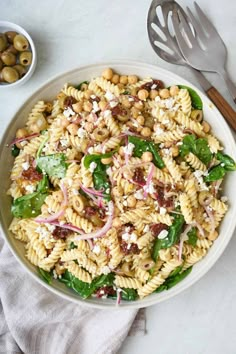 a white bowl filled with pasta salad next to olives