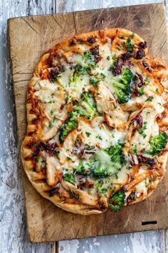 a pizza with broccoli and cheese on a cutting board next to a knife