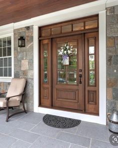 two chairs sitting on the front porch of a house with stone walls and wood doors