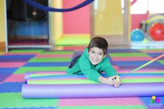 a young boy laying on top of a purple mat in a play room with colorful mats