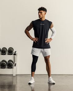 a man with his hands on his hips standing in front of a rack of dumbbells