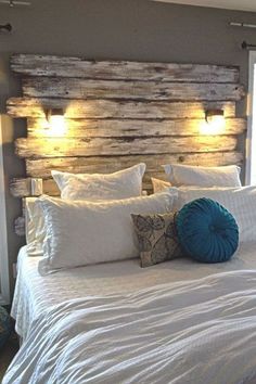 a bed with white sheets, pillows and lights on the headboard is made from wood planks