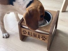 a dog eating food out of a wooden bowl on top of an elevated table with the word alma written across it