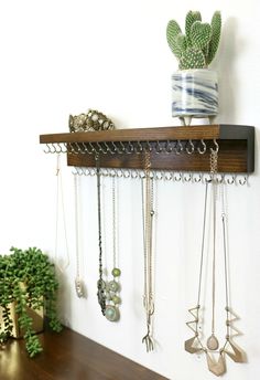 a wooden shelf with several necklaces hanging from it's sides and a potted plant in the background