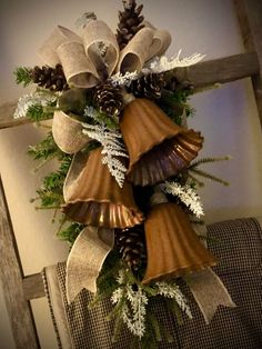 a christmas wreath with bells and pine cones hanging from the side of a wooden chair