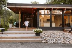 a woman walking up the steps to a modern house with glass doors and large windows