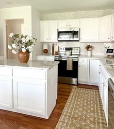 a kitchen with white cabinets and an island in the middle of the room, along with a rug on the floor